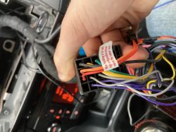 Ręka trzymająca wiązkę przewodów w samochodzie, widoczna kostka elektryczna z kolorowymi przewodami.