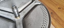 Metalowy bęben pralki z widocznym wałem i łożyskiem.