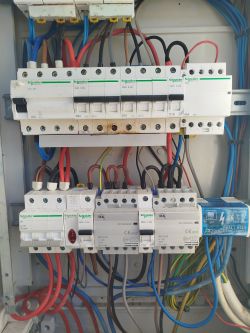 Widok wnętrza rozdzielnicy elektrycznej z zamontowanymi wyłącznikami marki Schneider Electric oraz widocznymi przewodami i śladami przepalenia pod jednym z wyłączników.