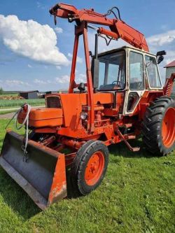 Orange JUMZ backhoe loader on grass, front-side view with crane arm visible.