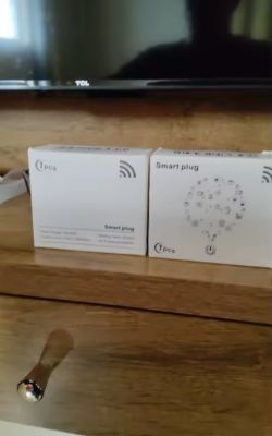 Two smart plug boxes on a wooden shelf below a TCL television