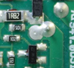 Fragment zielonej płytki drukowanej z elementami elektronicznymi i napisami.