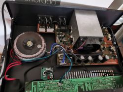 Wnętrze urządzenia elektronicznego z widocznym transformatorem toroidalnym, płytkami drukowanymi oraz wentylatorem.