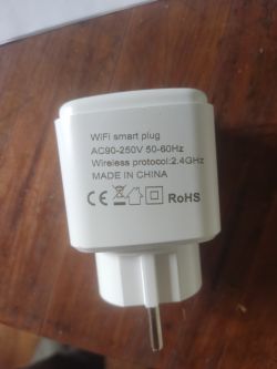White smart plug with technical markings, lying on a wooden surface.
