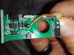 Energy metering PCB with BL0942 chip and wire Close-up of a green PCB with a circular hole and brown wire, showing a BL0942 chip, held between fingers