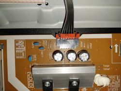 Fragment płytki drukowanej z podłączonym złączem przewodów, trzema kondensatorami i elementami elektronicznymi.
