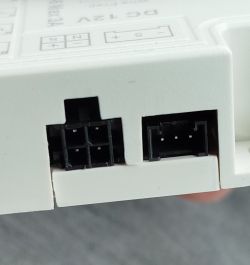 Zbliżenie białego zasilacza LED 12 V z dwoma czarnymi złączami na krawędzi obudowy