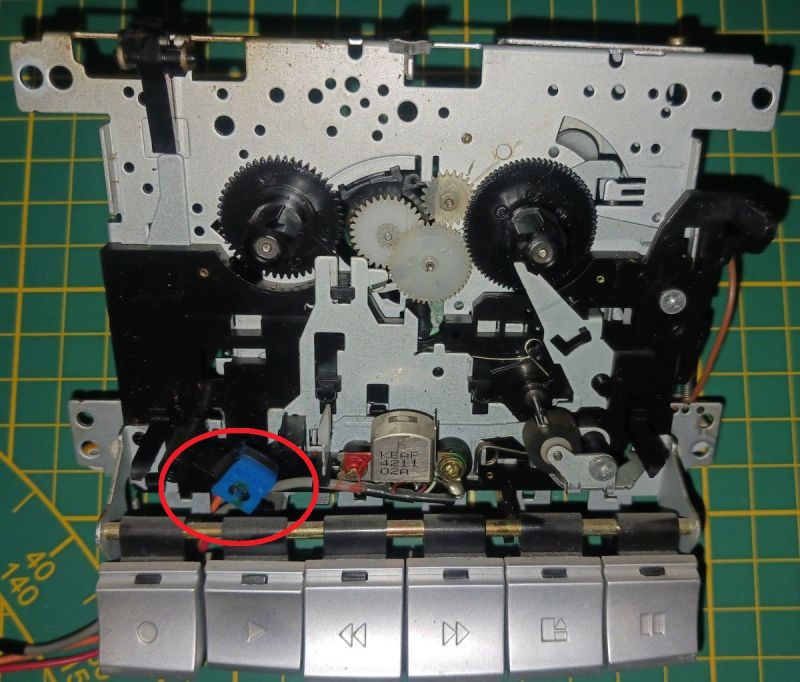 Mechanizm magnetofonu kasetowego z kołami zębatymi; czerwonym okręgiem zaznaczony niebieski element