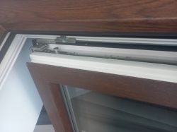 Detal zawiasu i mechanizmu uchylnego w oknie z ramą w okleinie drewnopodobnej