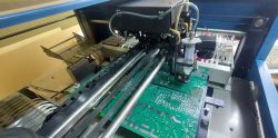 Automat montażowy M60 podczas pracy nad płytką PCB, widoczne podajniki i głowica montażowa.