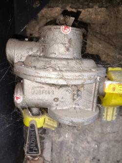 Zabrudzony reduktor gazowy z zaworem i dźwignią zabezpieczającą, w skrzynce instalacyjnej.