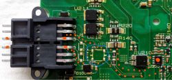 Close-up of a green printed circuit board with various electronic components, including a connector and a marked area.