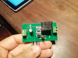 A hand holding a circuit board with a simple relay switch in a Sonoff case.