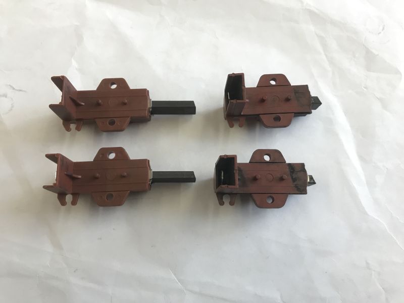 Four carbon motor brushes for a washing machine, two new and two worn, on a white background