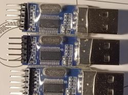 Three USB to TTL converters on a paper background with technical graphics and text.