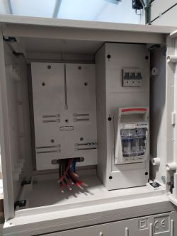 Wnętrze skrzynki z licznikami elektrycznymi z widocznymi kablami.