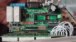 Zbliżenie na płytkę drukowaną z podzespołami elektronicznymi i białymi przewodami, widoczne przekaźniki Relpol oraz podstawki pod układy scalone.