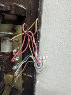 Zbliżenie na odsłoniętą instalację elektryczną domofonu z różnokolorowymi przewodami.