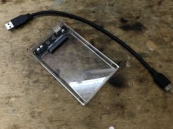 Przejściówka USB na SATA leży na drewnianym stole obok kabla USB.