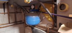 Pomieszczenie z instalacją grzewczą z widocznym niebieskim zbiornikiem i rurami.