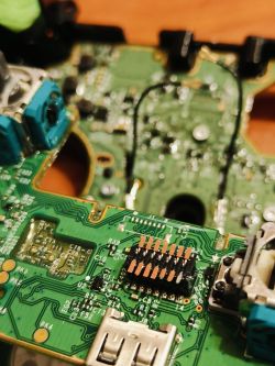 Zbliżenie na płytę główną zdemontowanego kontrolera Xbox z widocznymi komponentami elektronicznymi.