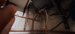 Widok na instalację hydrauliczną z rurami i zaworami w rogu pomieszczenia.