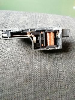 Zbliżenie na przekaźnik z widoczną cewką miedzianą na powierzchni tekstylnej.