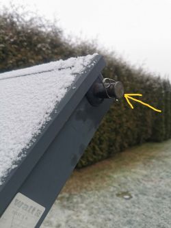 Zbliżenie na zaśnieżony kolektor słoneczny z zaznaczonym korkiem zaworu.
