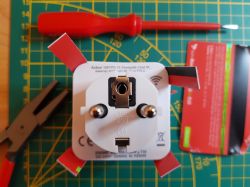 Electrical socket with adapter and credit card wedges, tools on a measuring mat background.