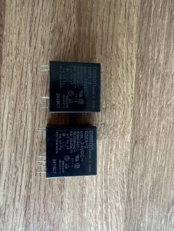 Dwa przekaźniki elektryczne Omron leżące na drewnianej powierzchni.