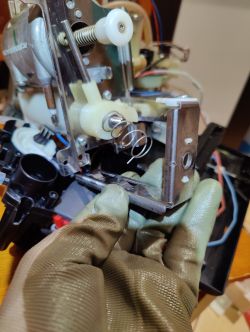 Ręka w rękawiczce trzyma metalowy uchwyt ze sprężyną pod urządzeniem elektro-mechanicznym
