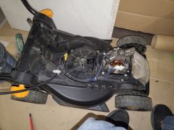 Widok od spodu na rozebraną kosiarkę elektryczną Ondragon z widocznym silnikiem i woreczkiem z piaskiem jako balastem.
