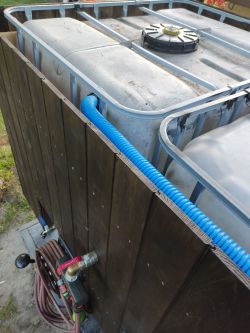 Rainwater storage tanks with a wooden cover and installed blue PVC pipe.