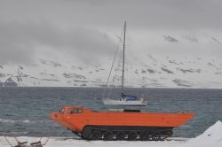 Amphibious Vehicle and Yacht in Arctic Landscape Orange amphibious vehicle and yacht in the background with snowy mountains.