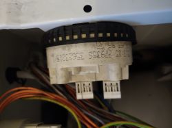 Zbliżenie na element elektroniczny w pralce z widocznymi kolorowymi przewodami.