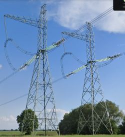 Dwa słupy wysokiego napięcia stojące na polu pod błękitnym niebem.