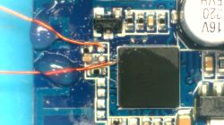 Close-up of a PCB with two thin wires soldered to specific pads and secured with glue.