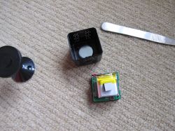 Disassembled Xiaomi X6 mini spy camera on carpet Disassembled mini spy camera with visible electronics and casing on a light brown carpet.