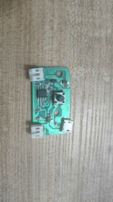 Mała zielona płytka PCB z przyciskiem, dwoma białymi złączami i portem micro‑USB na blacie