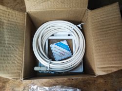 Open box with a coiled white cable and a device in plastic marked “Certificate of Quality”