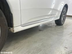 Part of the side of a white car, focusing on the side skirts and rear wheel.