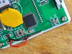 Close-up of a PCB with an IC chip, yellow battery cover, and red/black wires inside a casing