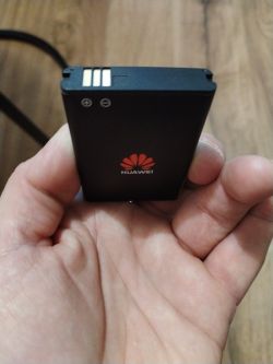 Bateria Huawei trzymana w dłoni, z widocznymi stykami zasilania i logotypem firmy