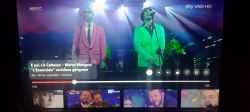 Screenshot z programu Sky UNO HD, pokazujący dwóch mężczyzn śpiewających na scenie, jeden w różowym garniturze, drugi w zielonym.