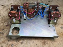 Interior of an old time relay: three brown relays, a central coil, and colored wiring on a metal base