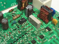 Zbliżenie na płytkę PCB programatora zmywarki z widocznymi elementami elektronicznymi, w tym układ TNY253GN, kondensatory, rezystory, cewki oraz przekaźnik.
