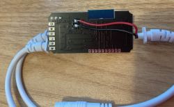 Opened LED Controller Circuit Board with Wires A black LED controller circuit board with connected wires, placed on a wooden surface.