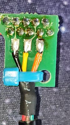 Zbliżenie płytki PCB z trzema przewodami (czarny, żółty, pomarańczowy) przylutowanymi do padów