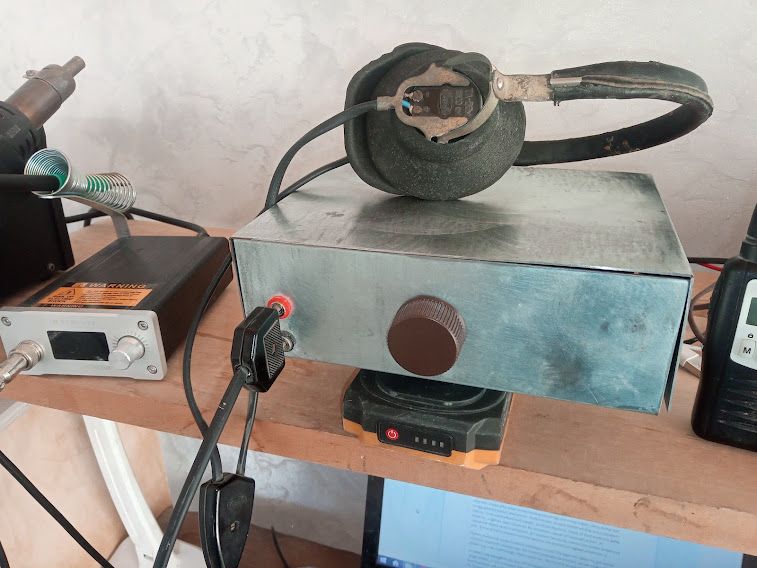 Domowe stanowisko z metalową skrzynką z pokrętłem i słuchawką na górze, na półce obok elektroniki.