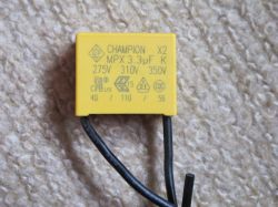 Yellow CHAMPION X2 MPX 3.3µF film capacitor on carpet background, with voltage ratings and certification marks.